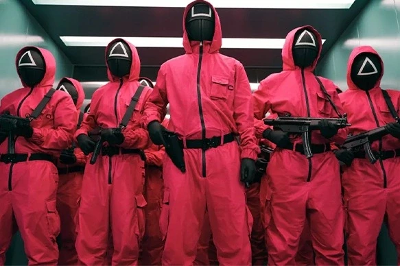 Masked guards in red suits holding guns in formation.