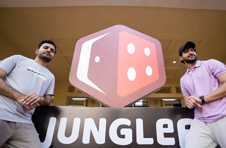 Two men posing beside Junglee logo signboard