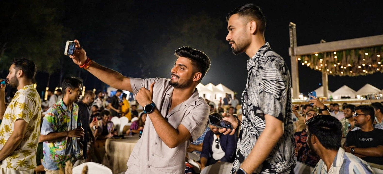 Two men taking a selfie at a lively outdoor event.