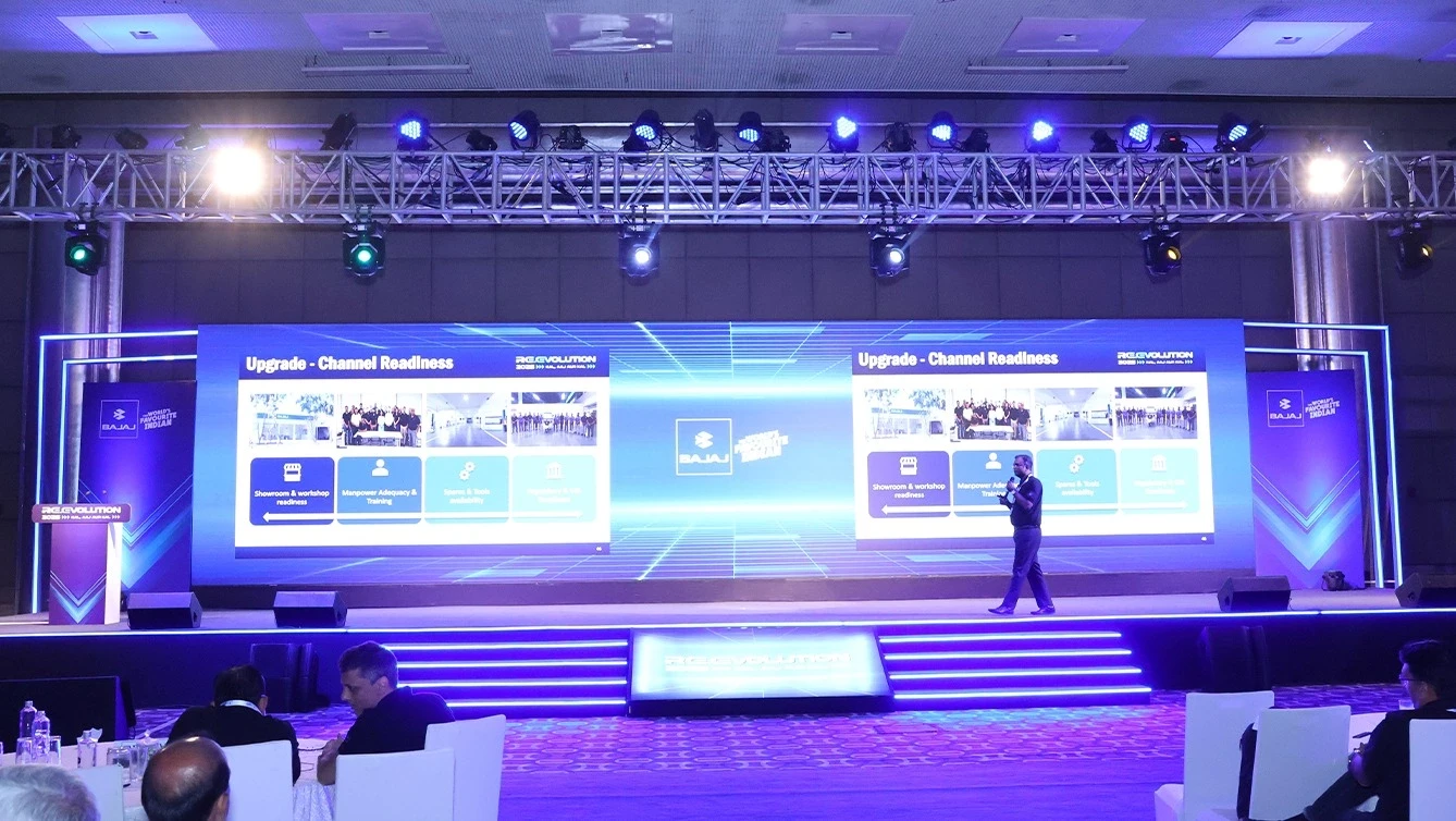 Speaker presenting at corporate event with large screen display.